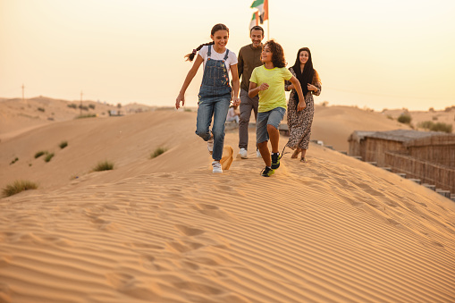 Happy Middle Eastern family running outdoors on the dunes of Dubai.