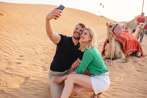 Caucasian tourists taking a fun selfie with the dromedary camel before the tour in Dubai.