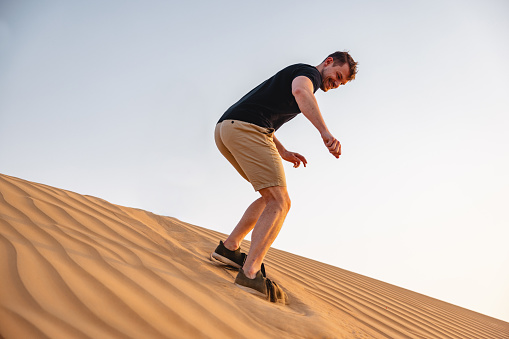 Focused shot of a young man sandboarding in the desert in Dubai.