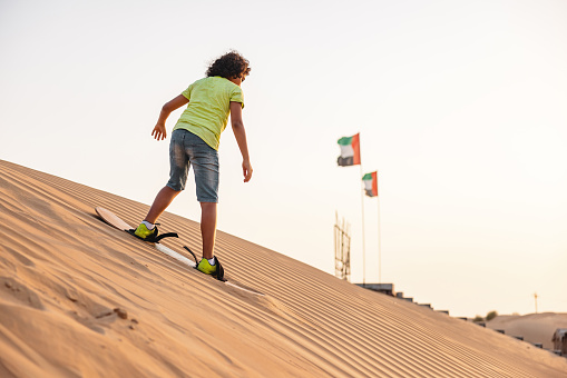 Young Middle Eastern girl sand boarding in the desert at sunny day in Dubai.