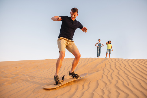 Portrait of a young tourist sandboarding in the desert in Dubai.
