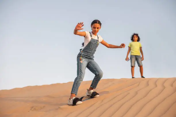 Teenage girls sandboarding  down the dunes of Dubai desert and having fun.