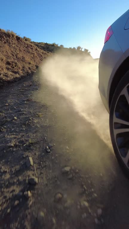 Car wheel spinning on mountain dusty road and sunset lights streaming POV