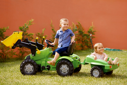 One and two years old babies play in the garden with a toy tractor.