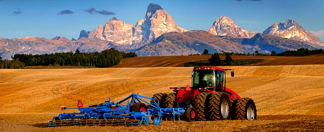 Tractor Equipment Farming Ground Harvesting crops in fall Autumn with Teton Mountains in background