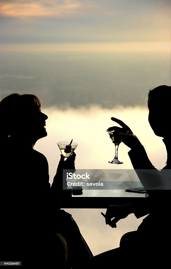 Couple having a drink in the sky Silhouette of a young couple drinking and having fun. Top floor skyscraper lounge window at sunset Cocktail Stock Photo