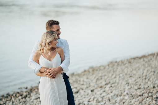 Couple on river beach after engagament, hugging, dressed in elegant summer outfit