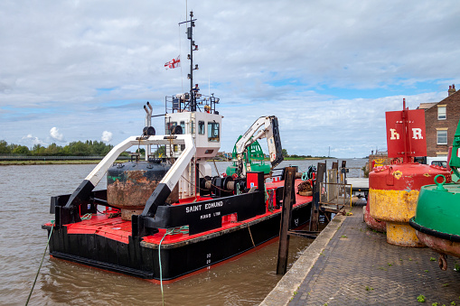 The King’s Lynn Conservancy Board buoy maintenance vessel, ‘St Edmund’, moored by Purfleet Quay, with various buoys on the quay and on the boat. The boat’s flag is flying at half-mast because of the recent death of Queen Elizabeth II.