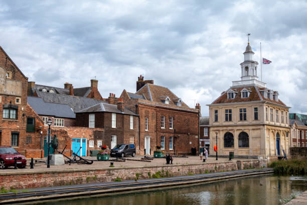 The Purfleet and old Custom House in King's Lynn A few people on the quayside of the Purfleet, an historic dock leading from the River Great Ouse in King’s Lynn, Norfolk, Eastern England, which is the site of the famous old Custom House. The Custom House is probably the best-known building in this ancient town and port on the west coast of Norfolk. It was built as a merchant exchange in 1683 on reclaimed land at Purfleet Quay in the Dutch style so often seen in Norfolk. The building was bought by the Crown in 1717 for the use of Customs officers and was in use in that capacity until 1989. The Union Flag is flying at half-mast in tribute to the late Queen Elizabeth II who had died a few days earlier. kings lynn stock pictures, royalty-free photos & images