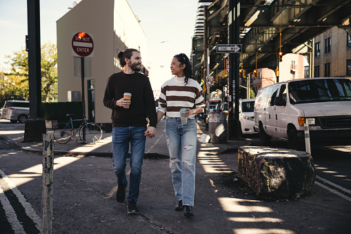 Happy couple in the streets of Bushwick in Brooklyn holding travel mug made by recycled material.