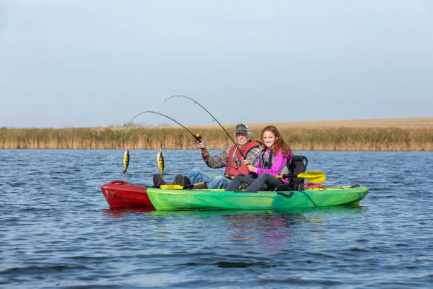 Grandfather & Granddaughter Kayak Fishing Grandfather and granddaughter kayak fishing on a beautiful autumn day on the water. Each of them has just caught a nice perch and is smiling at the camera. rowing boat fishing stock pictures, royalty-free photos & images