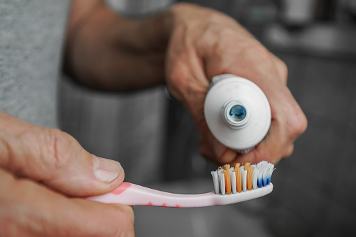 Old man with wrinkled hands squeezing paste to toothbrush close up view. Dental health care and hygiene concept.