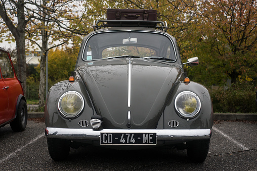 Mulhouse - France - 13 November 2022 - Front view of grey Volkswagen beetle with a leather suitcase on the roof  parked in the street