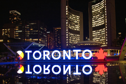 Toronto, Canada - August 11, 2022: Toronto sign lit up at night in Nathan Phillips Square with City Hall in the background.