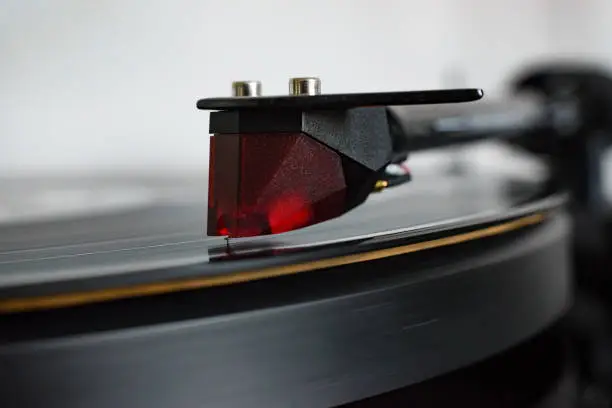 Closeup of a cartridge on a record player, vinyl playing with detail of stylus.