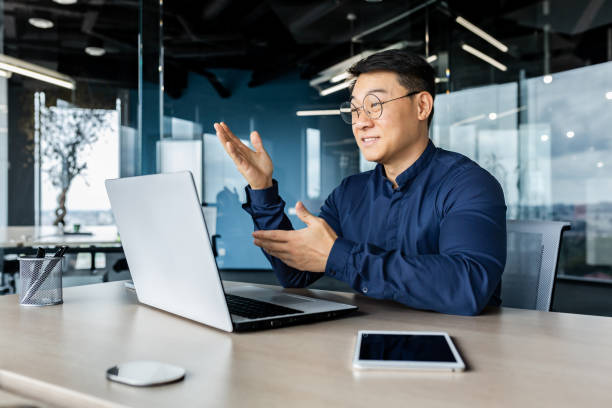 istock Successful Asian businessman talking on video call using laptop for remote communication with colleagues, boss in shirt smiling and gesturing with hands, online meeting with partners 1442290477