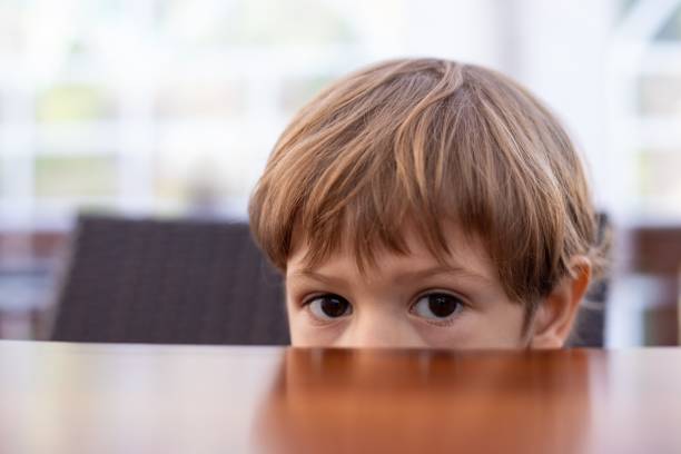istock Fearful little boy hide half face under wooden table in cafe hall closeup, free copy space. Pretty kid of kindergarten age scared to sit in kitchen. Morning, breakfast, phobia, alone 1442294679