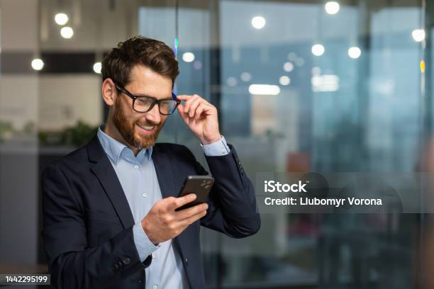 Successful Financier Investor Works Inside Office At Work Businessman In Business Suit Uses Telephone Near Window Man Smiles And Reads Good News Online From Smartphone Stock Photo - Download Image Now