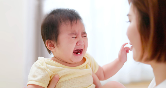 Close up shot - Asian baby crying mother trying to cheer up holding in hands at home