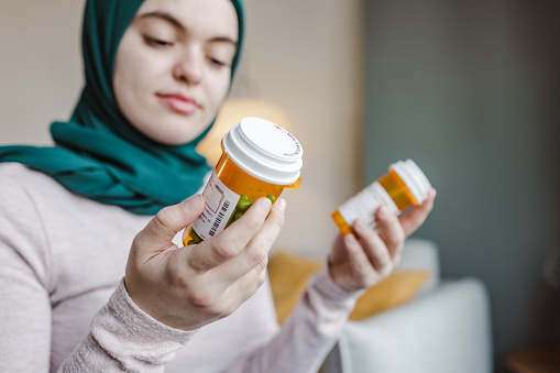 A young woman reading the label of the pill bottle at home