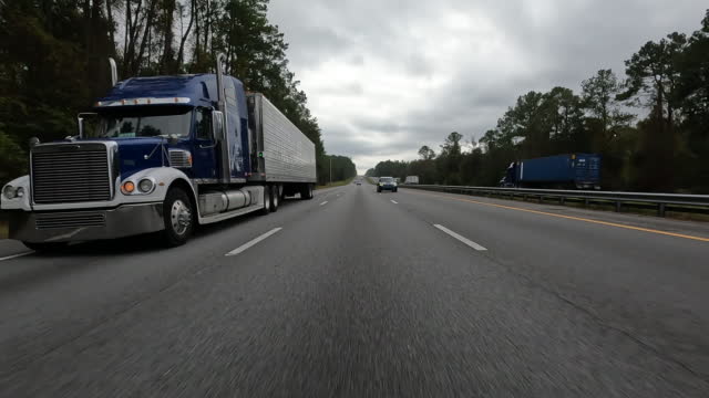 low angle rear view from vehicle, while passing by box trailer semi truck on Interstate highway