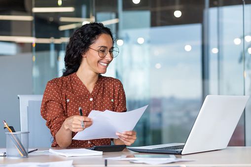 Successful satisfied and happy business woman working inside modern office, hispanic woman in glasses and shirt using laptop at work,