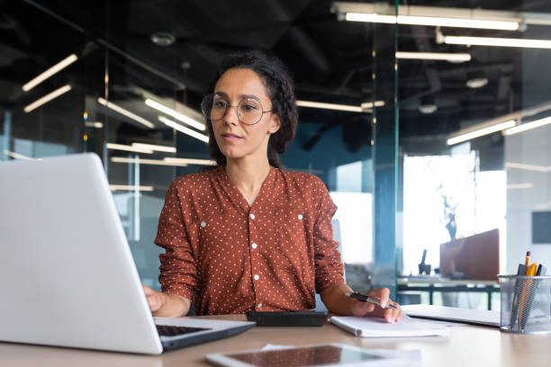 mulher de negócios satisfeita e feliz bem sucedida que trabalha dentro do escritório moderno, mulher hispânica em óculos e camisa usando laptop no trabalho - musical staff - fotografias e filmes do acervo