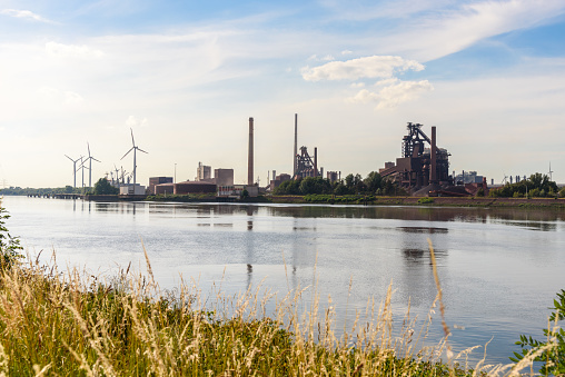 Large steel plant along a river on a sunny summer day. Wind turbines are visible in background. Bremen, Germany