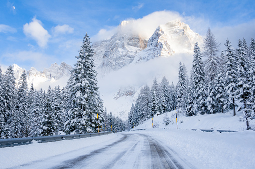 Icy road running through a snowy forest at the foot of a towering mountain on a clear winter day