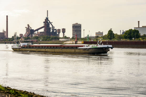 istock Cargo barge sailing past a large riverside steel plant at sunset 1442307122