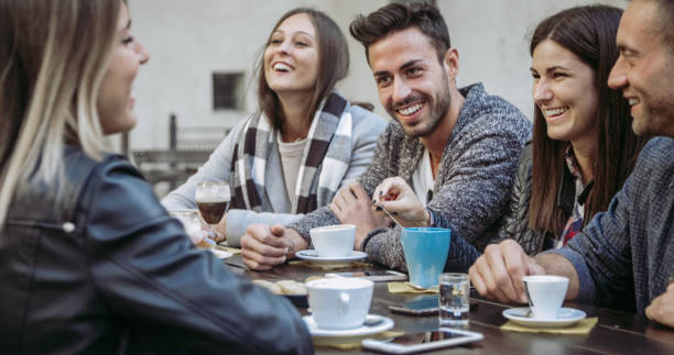 People tasting hot drinks at coffee restaurant  - Millennial friends talking and having fun together at sidewalk cafe - Life style concept with happy men and women at bar cafeteria stock photo