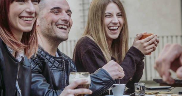 People tasting hot drinks at coffee restaurant  - Millennial friends talking and having fun together at sidewalk cafe - Life style concept with happy men and women at bar cafeteria stock photo