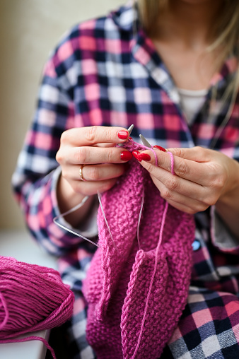 Woman crocheting with threads at grey table, closeup. Engaging hobby