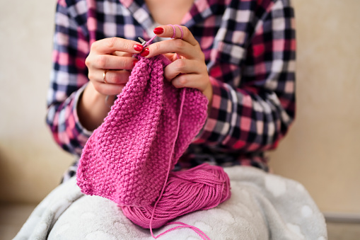 young woman knitting sweater while sitting on the sofa.