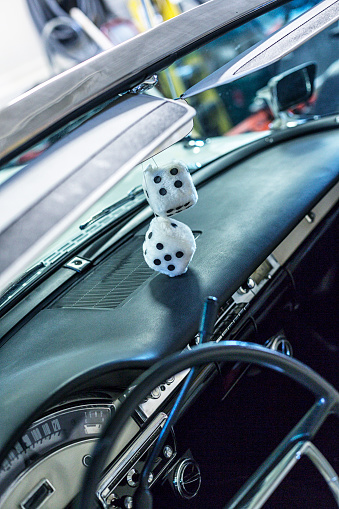 Close-up details shot of a classic collector's car 1950's (1957)  convertible parked before a photo shoot. This one features an overhead view of the windshield below the upturned sun visors, dashboard and steering wheel with two white with black polka dots iconic dice hanging from the car's interior rear-view mirror.