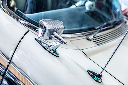 Close-up detail shot of the passenger side classic custom bullet style outside rear view mirror and aerodynamic base radio antenna on the front fender of a late 1950's collector's car (1957) convertible.