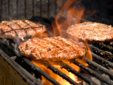 Summer barbequed burgers with flames. Shallow DOF (focus on the center of the front burger).