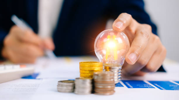 istock Business man hand holding lightbulb with using calculator to calculate and money stack. idea saving energy and accounting finance in office concept. Financial statistics, infographics papers. 1442316171