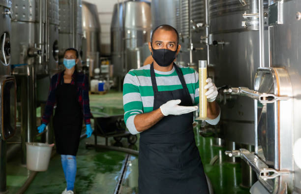 istock Winemaker in mask checking wine at factory 1442317483