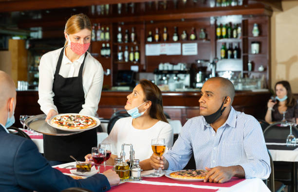istock Waitress in protective mask serving pizza to guests in restaurant 1442317546