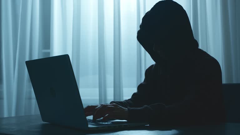 Silhouette of a hacker in a hood sitting at a laptop. Cyber attack.