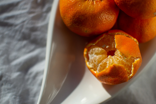A group of ripe orange tangerines on a white plate on a white sheet