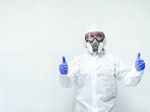 man wearing a protective suit and face mask with the thumbs up