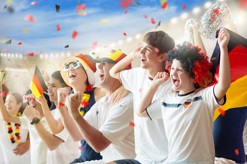 Germany football supporter on stadium. German fans on soccer pitch watching team play. Group of supporters with flag and national jersey cheering for Germany. Championship game.
