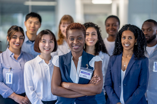 A large group of mature business professionals stand together for a portrait.  They are each dressed professionally and are smiling.