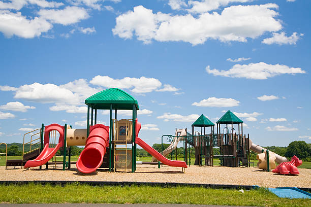 Distant view of a Colorful playground structure in a residential area park, with spring dandelions under a stormy sky
