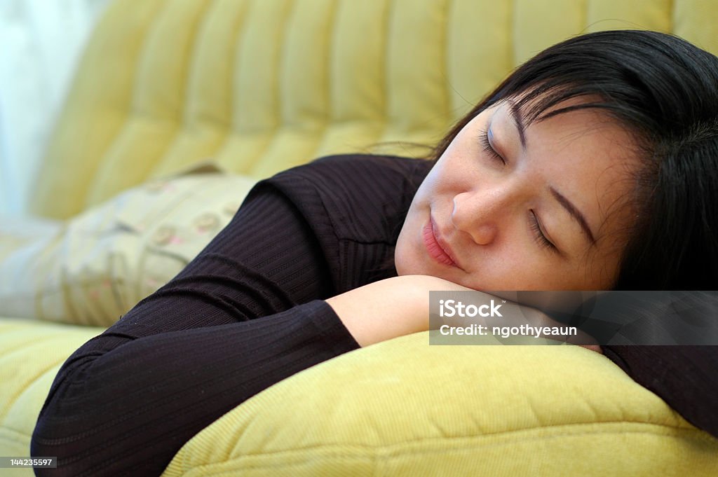 Closeup of a woman sleeping on a large yellow cushion A chinese asian lady fall asleep on sofa at home. Adult Stock Photo