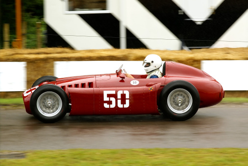 A 1954 Lancia D50 open-wheel single-seater racing car car being driven in wet weather at the Goodwood Festival of Speed.