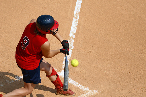 Young lady on a High School softball team swinging at the ball.