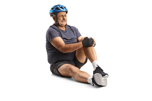 Mature bicycle rider sitting on the ground and holding his knee isolated on white backgroundd